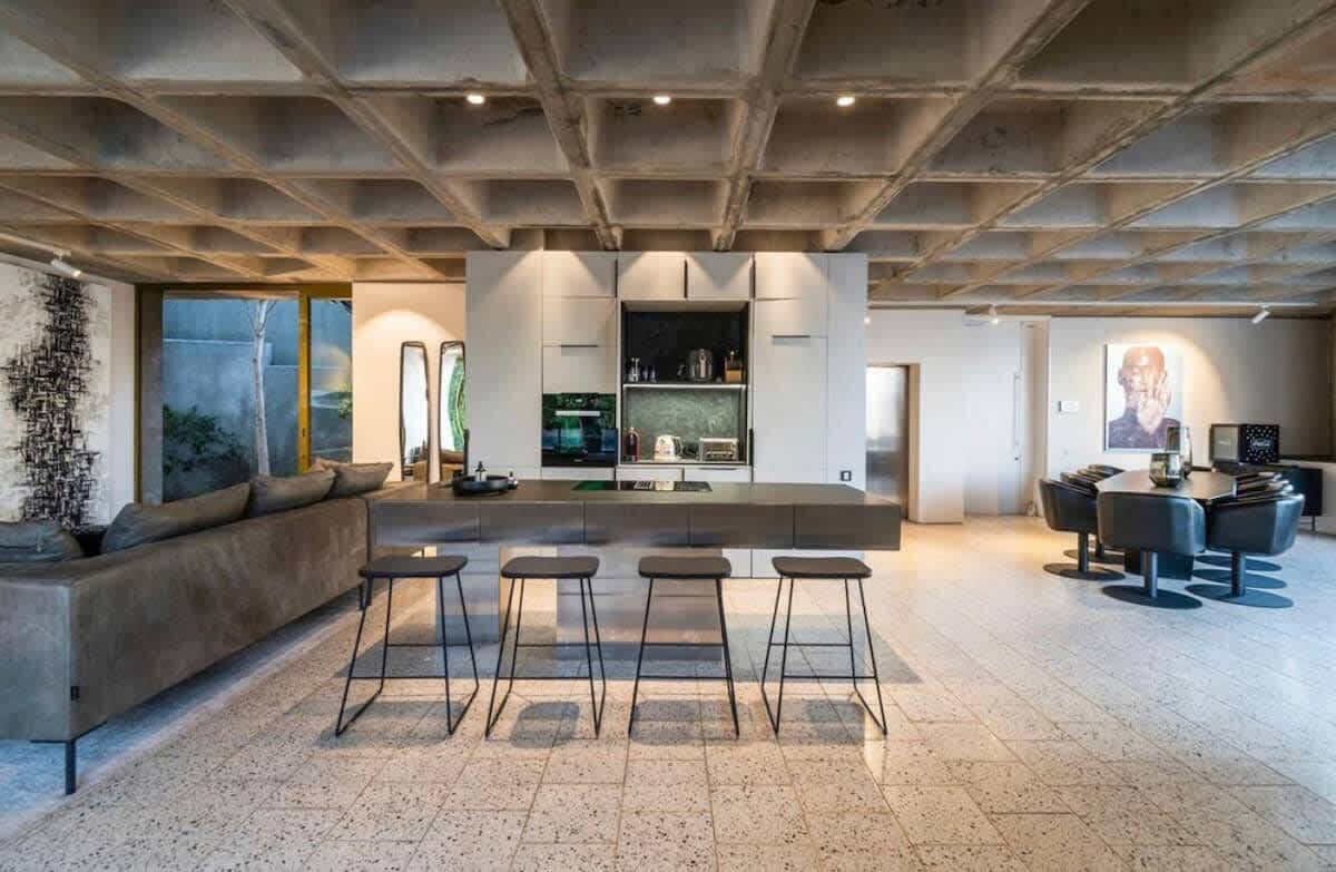Una cocina moderna con una isla central, taburetes de bar y un comedor con una mesa redonda.