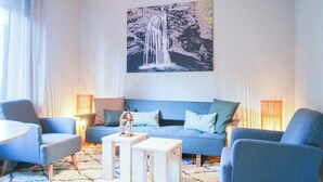 Un soggiorno moderno con un divano blu, due poltrone, un tavolino da caffè e un quadro raffigurante una cascata al muro.