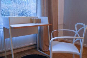 Een kamer met een witte radiator, een raam met gordijnen, een witte stoel en een houten plank met een metalen voorwerp.