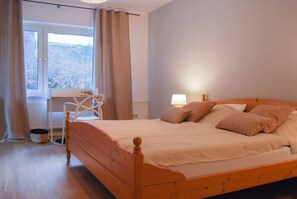 Een slaapkamer met een houten bed, een raam met gordijnen, een radiator en een lamp op het nachtkastje.