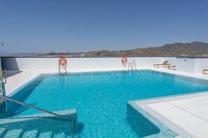 Ein Dachpool mit klarem, blauem Wasser, zwei Rettungsringen und Blick auf ferne Hügel.