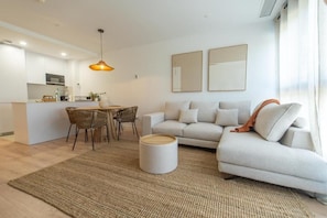 A modern living room with a sofa, a dining area with chairs, a coffee table, and a kitchen in the background. - Málaga City-View 2BR · Pool, Gym & Free Parking (Málaga)
