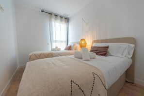 Ein Schlafzimmer mit zwei Betten, einem Fenster mit Vorhängen, einer Nachttischlampe und einer Wandleuchte.