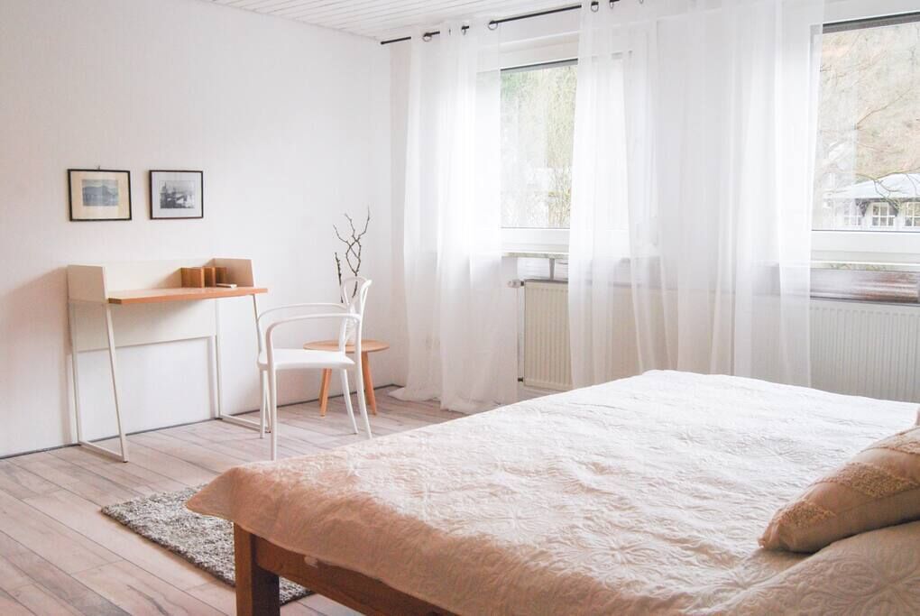 Ein Schlafzimmer mit Bett, Sessel, Schreibtisch und Heizkörper.