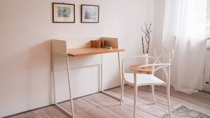 Ein schlicht eingerichteter Raum mit einem Holztisch, einem weißen Stuhl und zwei gerahmten Bildern an der Wand.