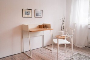 Ein schlicht eingerichteter Raum mit einem Holztisch, einem weißen Stuhl und zwei gerahmten Bildern an der Wand.