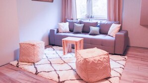 Ein Wohnzimmer mit grauem Sofa, zwei Hocker, einem kleinen Holztisch und einem gemusterten Teppich.