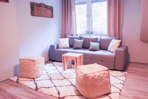 Ein Wohnzimmer mit grauem Sofa, zwei Hocker, einem kleinen Holztisch und einem gemusterten Teppich.