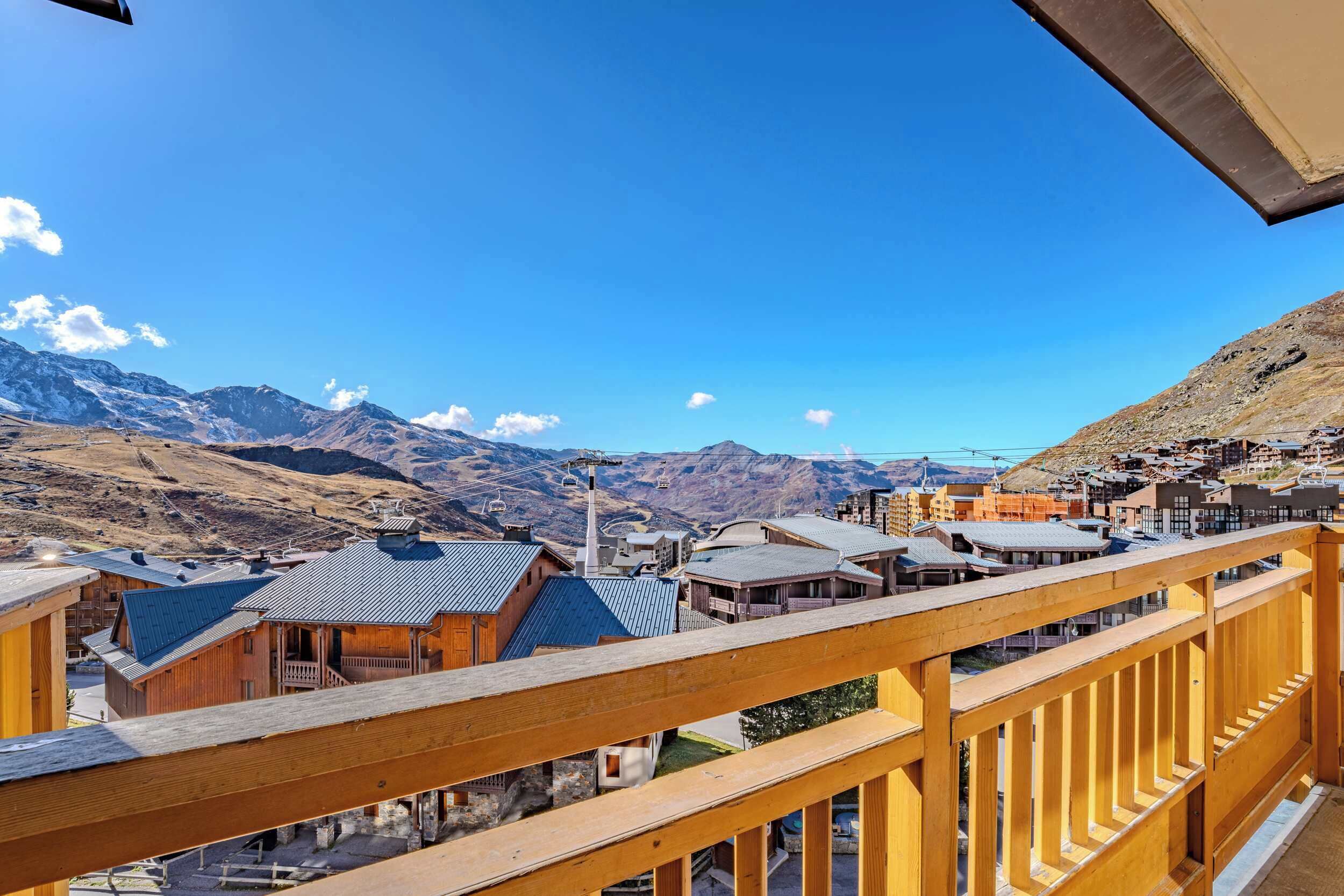 Een houten balkon met uitzicht op een bergachtig landschap met gebouwen en een heldere lucht.