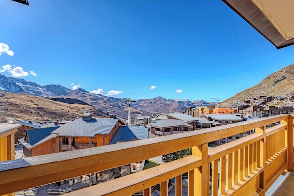 Ein hölzerner Balkon mit Blick auf eine gebirgige Landschaft, mit Gebäuden und klarem Himmel.
