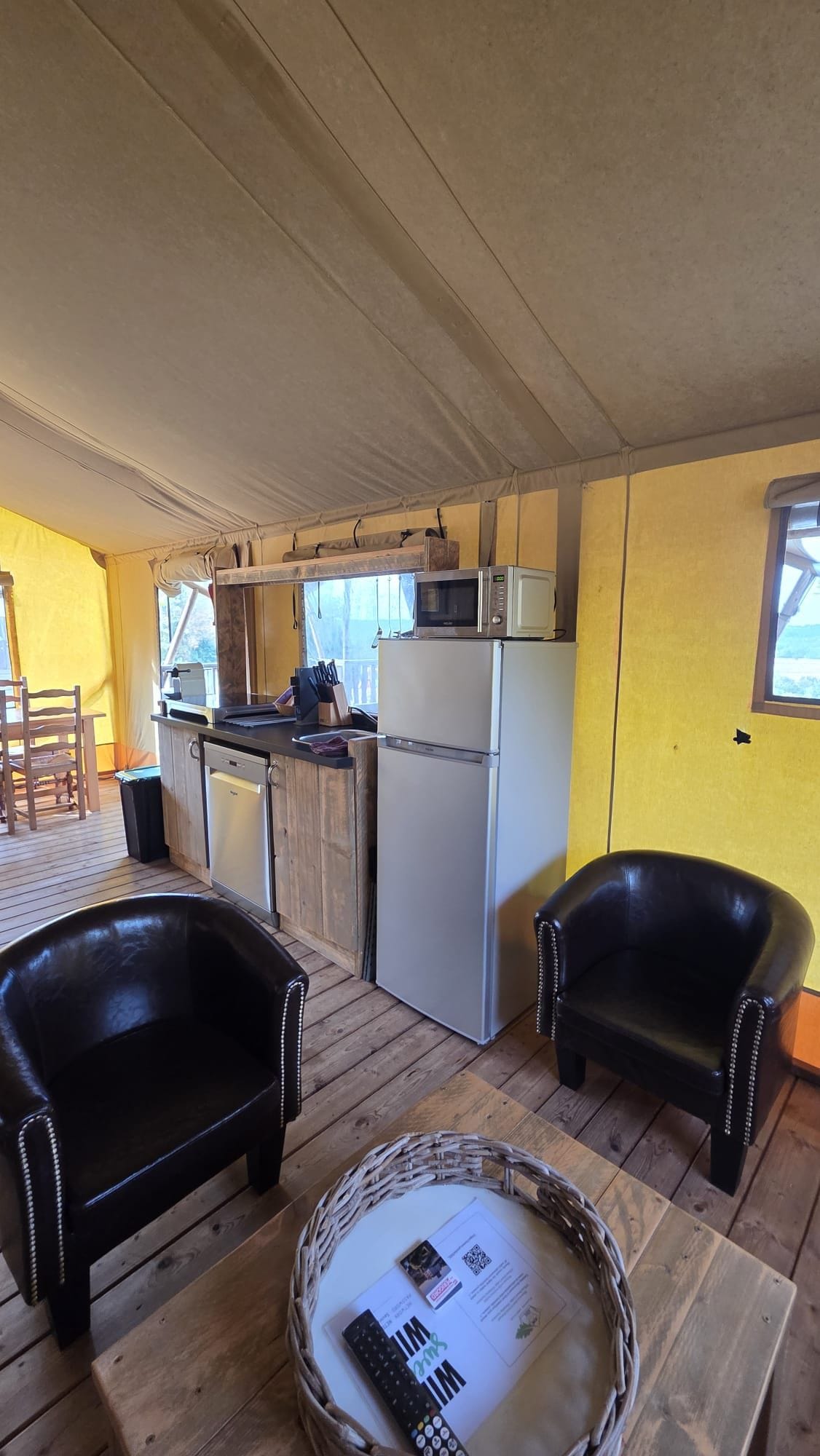 Un espacio habitable compacto con kitchenette, dos sillones, una mesa de comedor y una cesta con un control remoto.