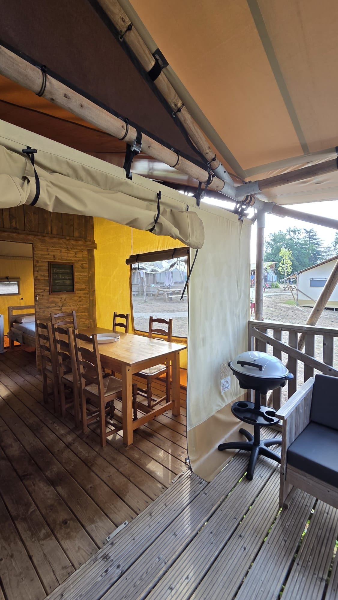 Una terraza de madera con mesa y sillas, una parrilla y una zona cubierta con vistas al exterior.
