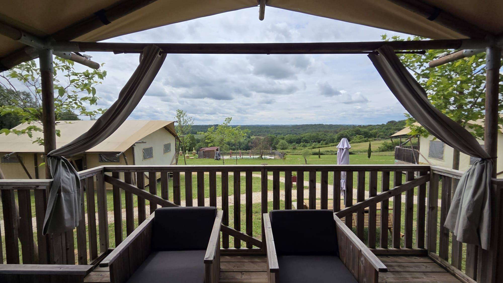 Un espacio de estar al aire libre con techo y vistas a un paisaje verde y edificios a la distancia.