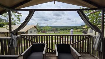 Un espacio de estar al aire libre con techo y vistas a un paisaje verde y edificios a la distancia.