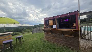 An outdoor bar with a wooden structure, a green umbrella, and a view of the landscape.