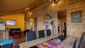 A wooden interior with a dining table, chairs, a coffee machine, and a chalkboard with a welcome message.