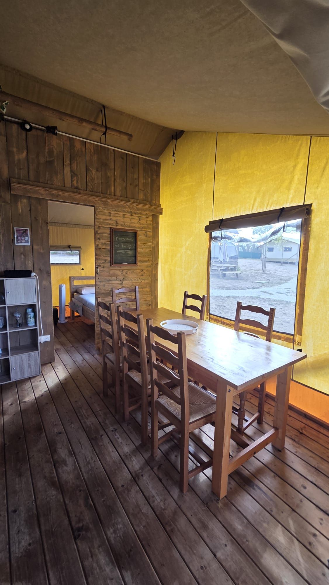 A wooden interior with a dining table and chairs, a bunk bed, and a window with a view of the outside.