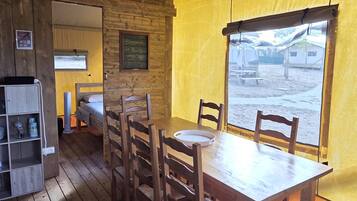 A wooden interior with a dining table and chairs, a bunk bed, and a window with a view of the outside.
