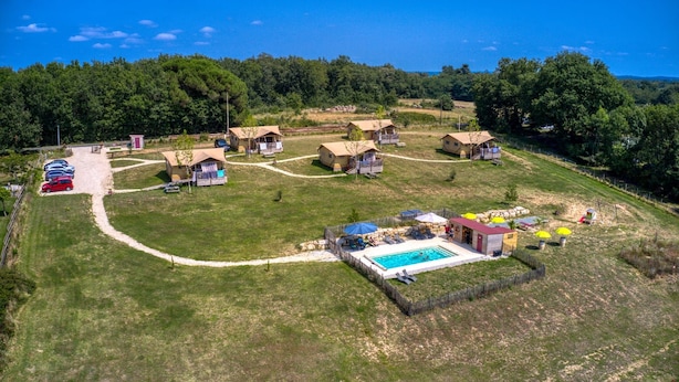 An aerial view of a campsite with multiple tents, a swimming pool, and a parking area.