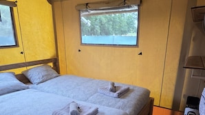 A single bed with a wooden frame and a textured white bedspread, a window with a view of trees, and a portable heater on the floor.