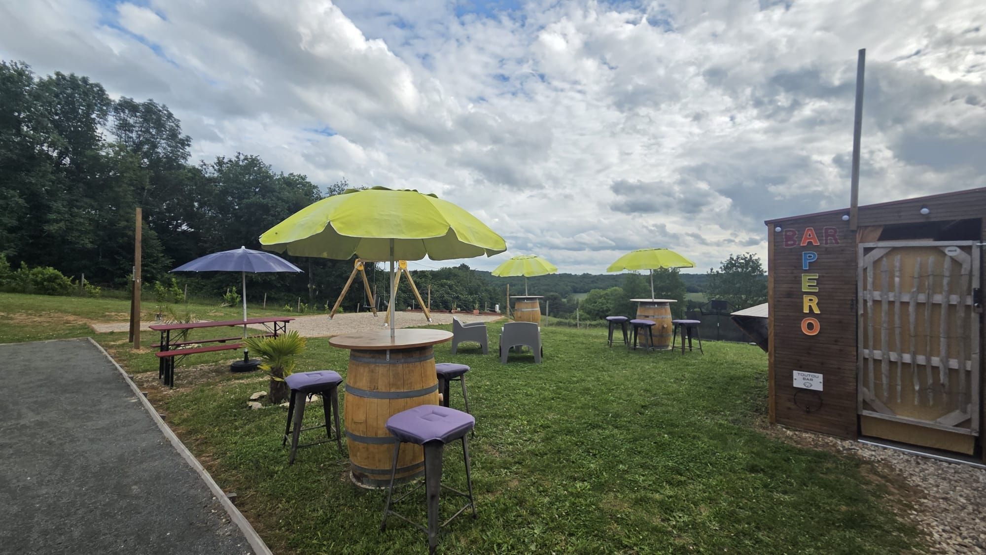 Un espace extérieur aménagé avec des tables et des chaises rondes, entouré de barils en bois et agrémenté de parasols.