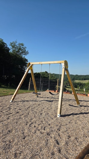 A wooden swing set on a gravel surface with a clear blue sky in the background.