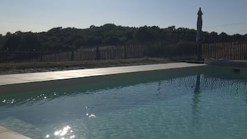 A swimming pool with clear water, surrounded by a tiled deck and a wooden fence.