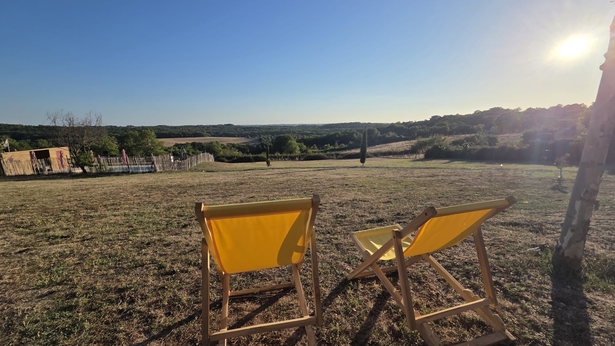 Two yellow chairs facing a grassy field with a clear sky and distant hills.