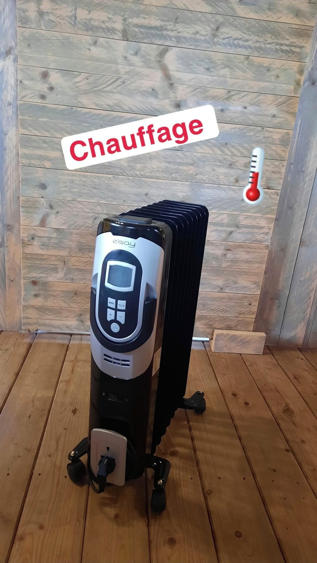 Un appareil de chauffage portatif doté d’un panneau de commande, placé sur un plancher en bois dans une pièce dont un des murs est également en bois.