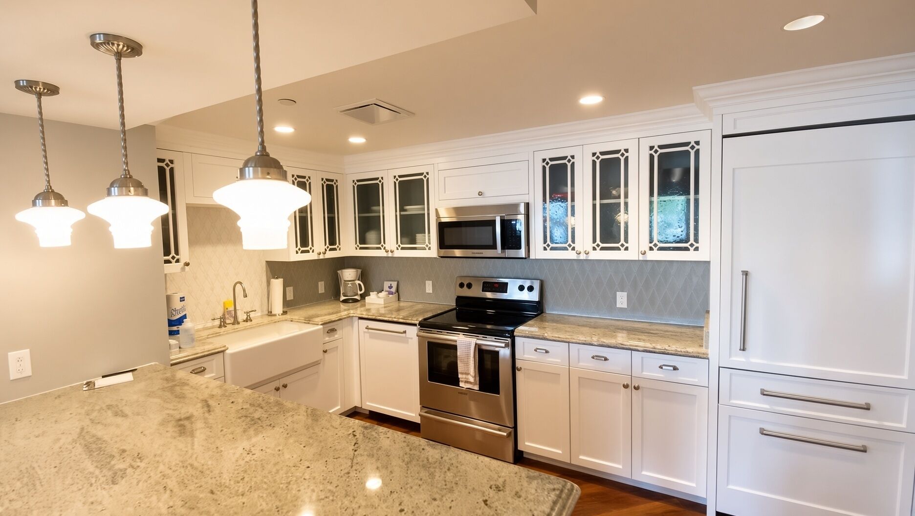 A modern kitchen with white cabinetry, stainless steel appliances, and pendant lighting.