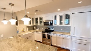 Una cucina moderna con mobili bianchi, elettrodomestici in acciaio inossidabile e luci a sospensione.