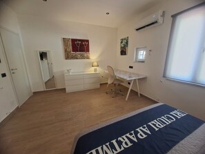 Ein Schlafzimmer mit einem Bett, einem Schreibtisch, einem Stuhl, einer Kommode und einem Fenster.