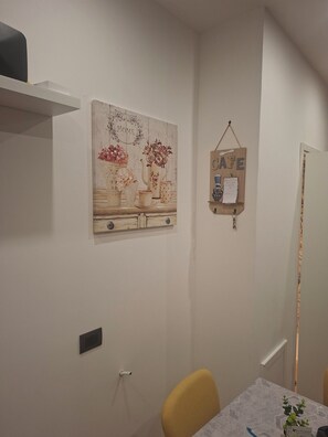 Un espace repas comprenant une table, des chaises, une étagère fixée au mur et un tableau décoratif.