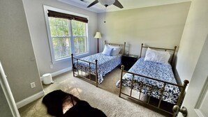 Ein Schlafzimmer mit zwei Betten, einem Deckenventilator, einem Fenster mit Vorhängen und einem Teppichboden.