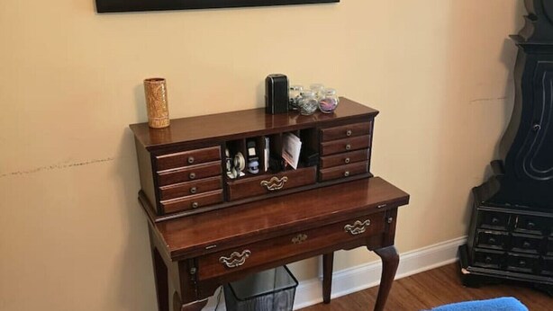Ein Zimmer mit Schreibtisch aus Holz, einem Sessel, einem gerahmten Bild an der Wand und einer großen Uhr.