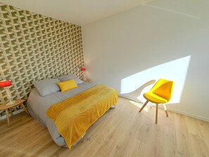 A modern bedroom with a geometric-patterned headboard, a bed with a yellow throw, a bright yellow chair, and a small bedside table with a lamp. - Holiday Home in Brittany With Sea View (Cleder)