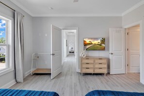 A bedroom with a bed, a dresser, a television, and a door leading to another room. - Rosemary Villa, Heated Saltwater Pool, Volleyball Court, Golf Cart, Main ST (North Myrtle Beach)
