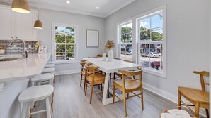 A modern kitchen with a central island, bar stools, and large windows offering a view of the street. - Rosemary Villa, Heated Saltwater Pool, Volleyball Court, Golf Cart, Main ST (North Myrtle Beach)