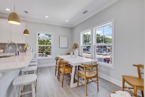 A modern kitchen with a central island, bar stools, and large windows offering a view of the street. - Rosemary Villa, Heated Saltwater Pool, Volleyball Court, Golf Cart, Main ST (North Myrtle Beach)