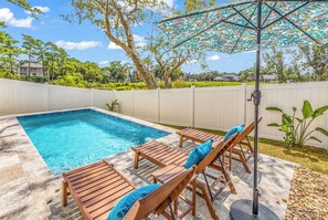 A backyard with a swimming pool, wooden lounge chairs, and a patio umbrella. - Rosemary Villa, Heated Saltwater Pool, Volleyball Court, Golf Cart, Main ST (North Myrtle Beach)