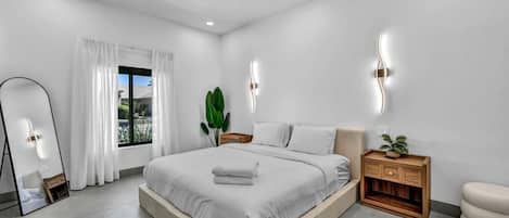 Une chambre à coucher moderne avec un grand lit, des tables de chevet, un miroir et une vue sur l’extérieur.