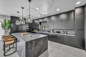 A modern kitchen with a large island, dark cabinetry, and pendant lighting. - The signature Luxury Las Vegas Getaway (Las Vegas)
