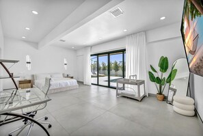 Ein modernes Hotelzimmer mit Bett, Schreibtisch, Glastisch, großem Fenster und Blick ins Freie.