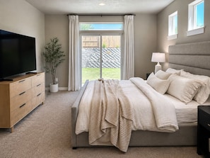 Une chambre à coucher avec un lit, une télévision, une plante et une fenêtre avec des rideaux.