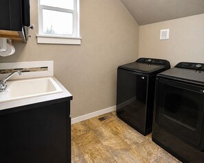Une buanderie équipée de deux machines à laver et deux sèche-linge noirs, d’un évier et d’une fenêtre.