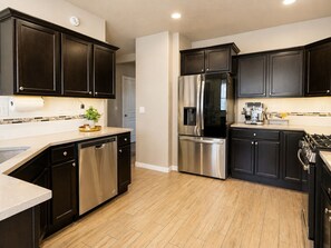 Une cuisine moderne avec des meubles de couleur sombre, des appareils en acier inoxydable et un plancher en bois.