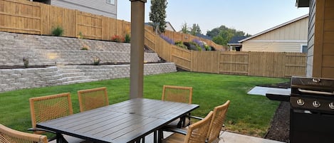 An outdoor patio with a table and chairs, a grill, and a stone retaining wall.