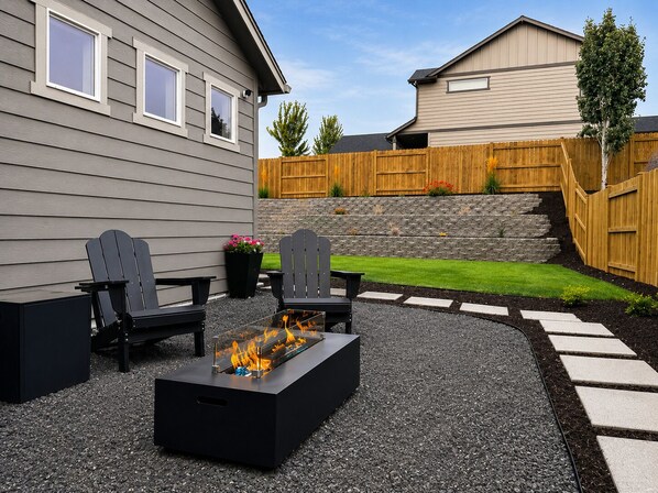 A backyard with a fire pit, two Adirondack chairs, and a stone wall.