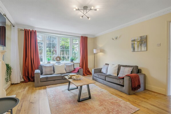 A living room with a grey sofa set, a coffee table, and a large window with curtains.