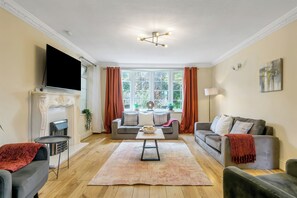 A living room with a fireplace, a flat-screen TV, a sofa, a coffee table, and a large window with curtains.